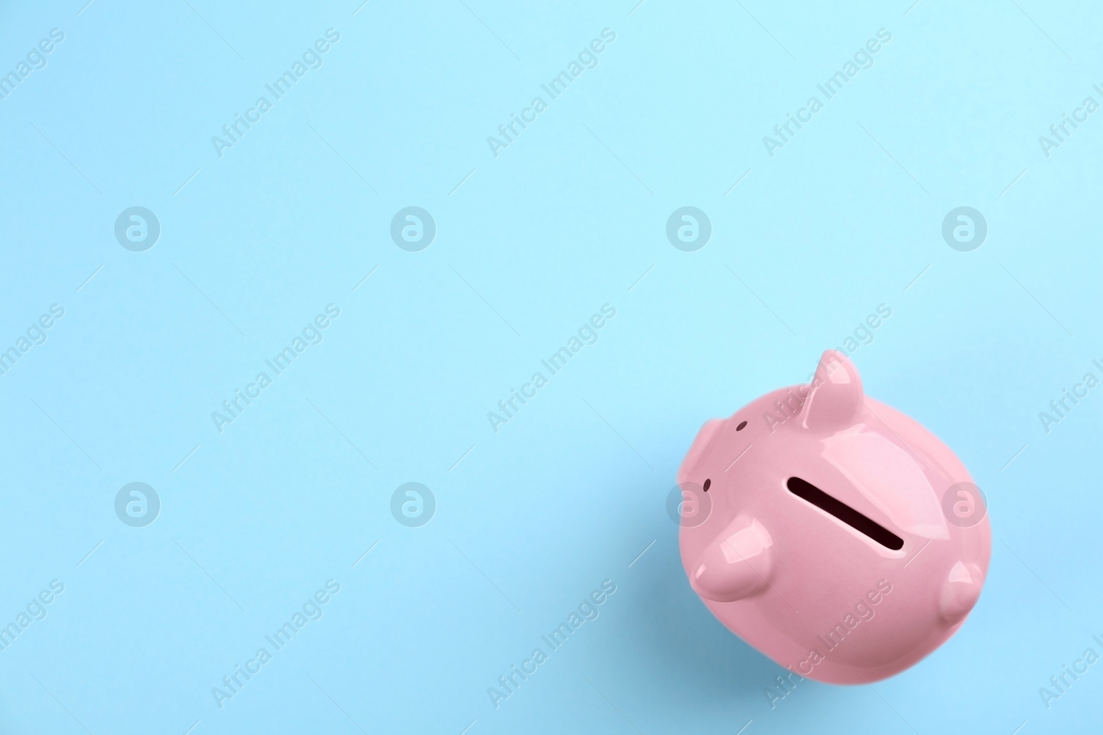 Photo of Pink piggy bank on light blue background, top view. Space for text