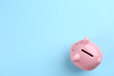Pink piggy bank on light blue background, top view. Space for text