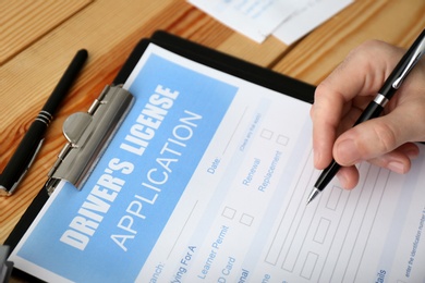 Photo of Man filling in driver's license application form at wooden table, closeup