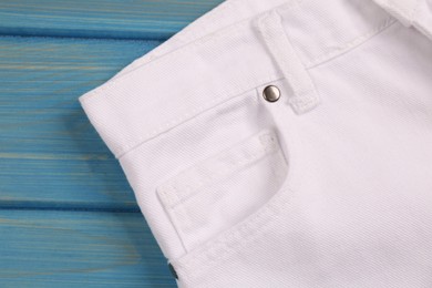Photo of Stylish white jeans on light blue wooden background, closeup of inset pocket