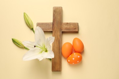 Photo of Wooden cross, painted Easter eggs and lily flowers on pale yellow background, flat lay