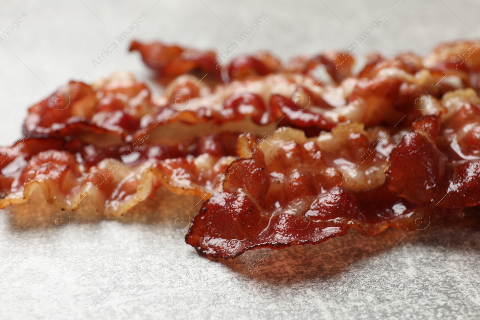 Photo of Pieces of tasty fried bacon on gray textured table, closeup