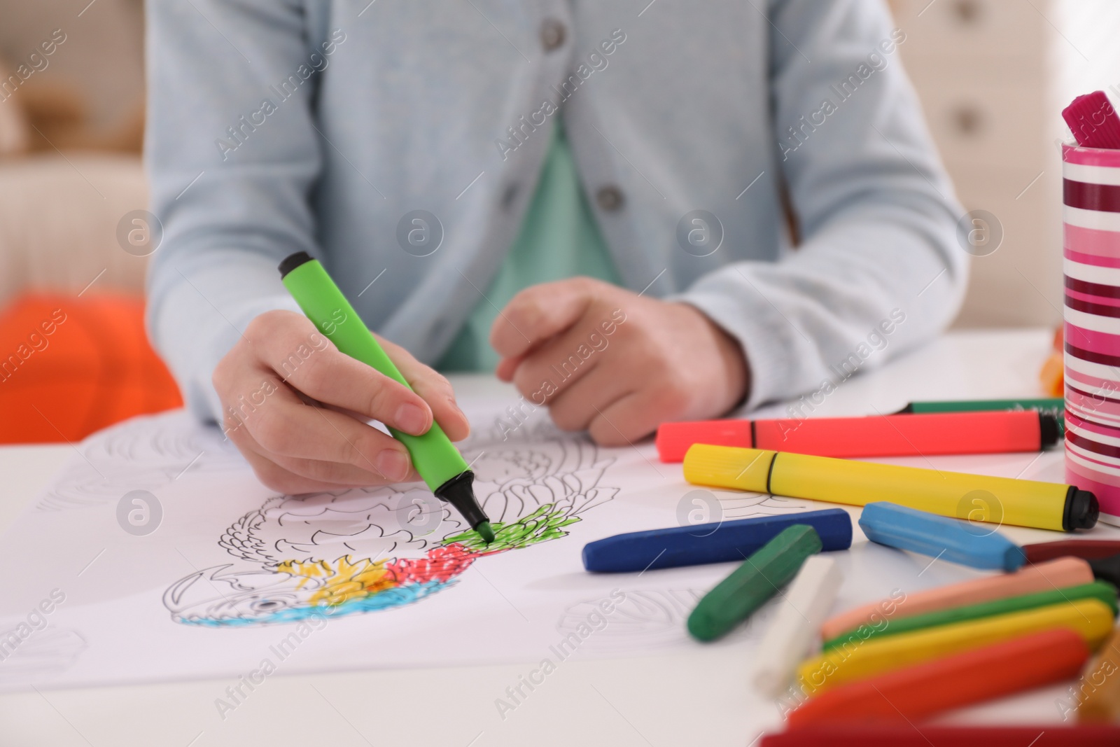 Photo of Child coloring drawing at table in room, closeup