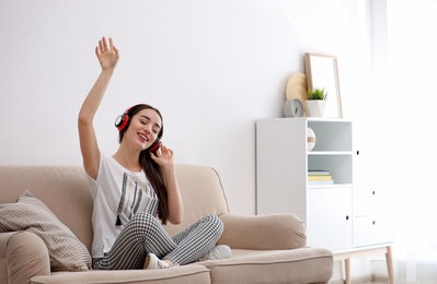 Photo of Young woman in headphones enjoying music on sofa at home