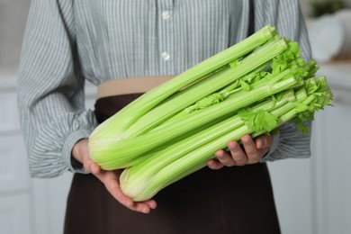Photo of Woman with fresh green celery in kitchen, closeup