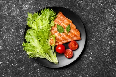 Photo of Tasty grilled salmon with tomatoes and fresh lettuce on black table, top view