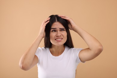 Emotional woman examining her hair and scalp on beige background