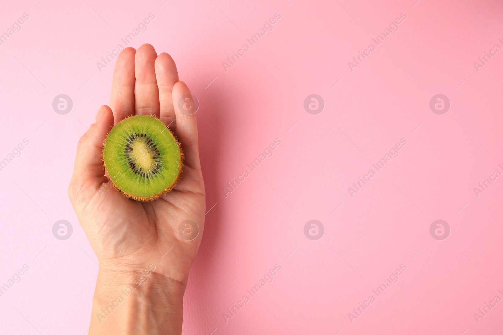Photo of Woman holding delicious fresh kiwi on pink background, top view. Space for text