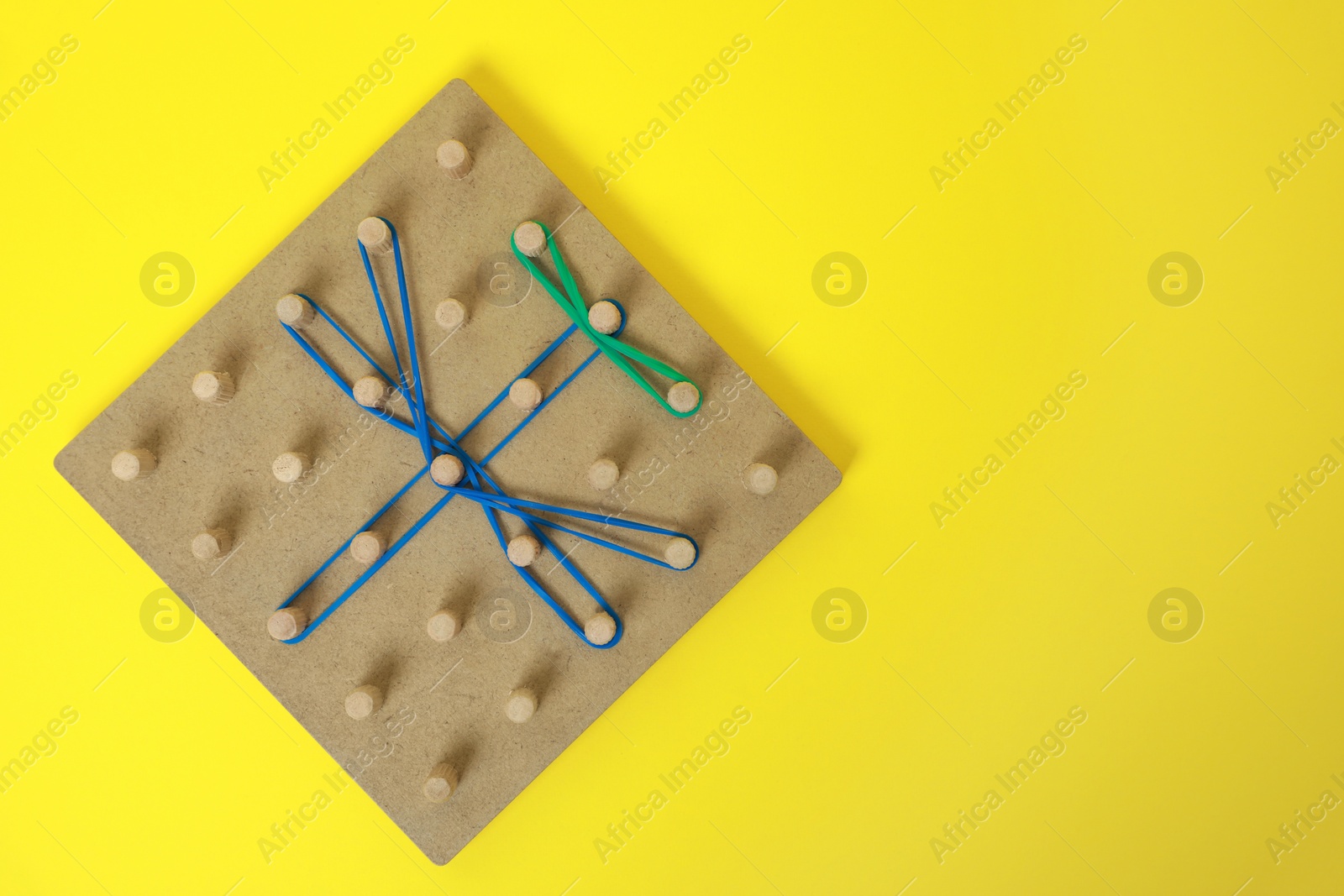 Photo of Wooden geoboard with dragonfly shape made of rubber bands on yellow background, top view and space for text. Educational toy for motor skills development
