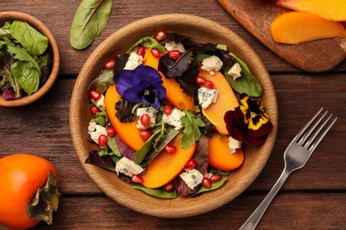 Photo of Delicious persimmon salad with cheese and pomegranate served on wooden table, flat lay