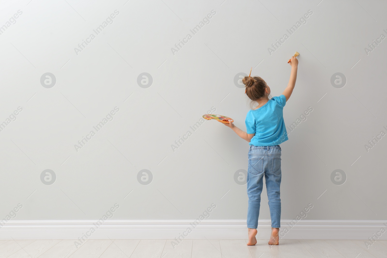 Photo of Little girl painting on light grey wall indoors, back view. Space for text