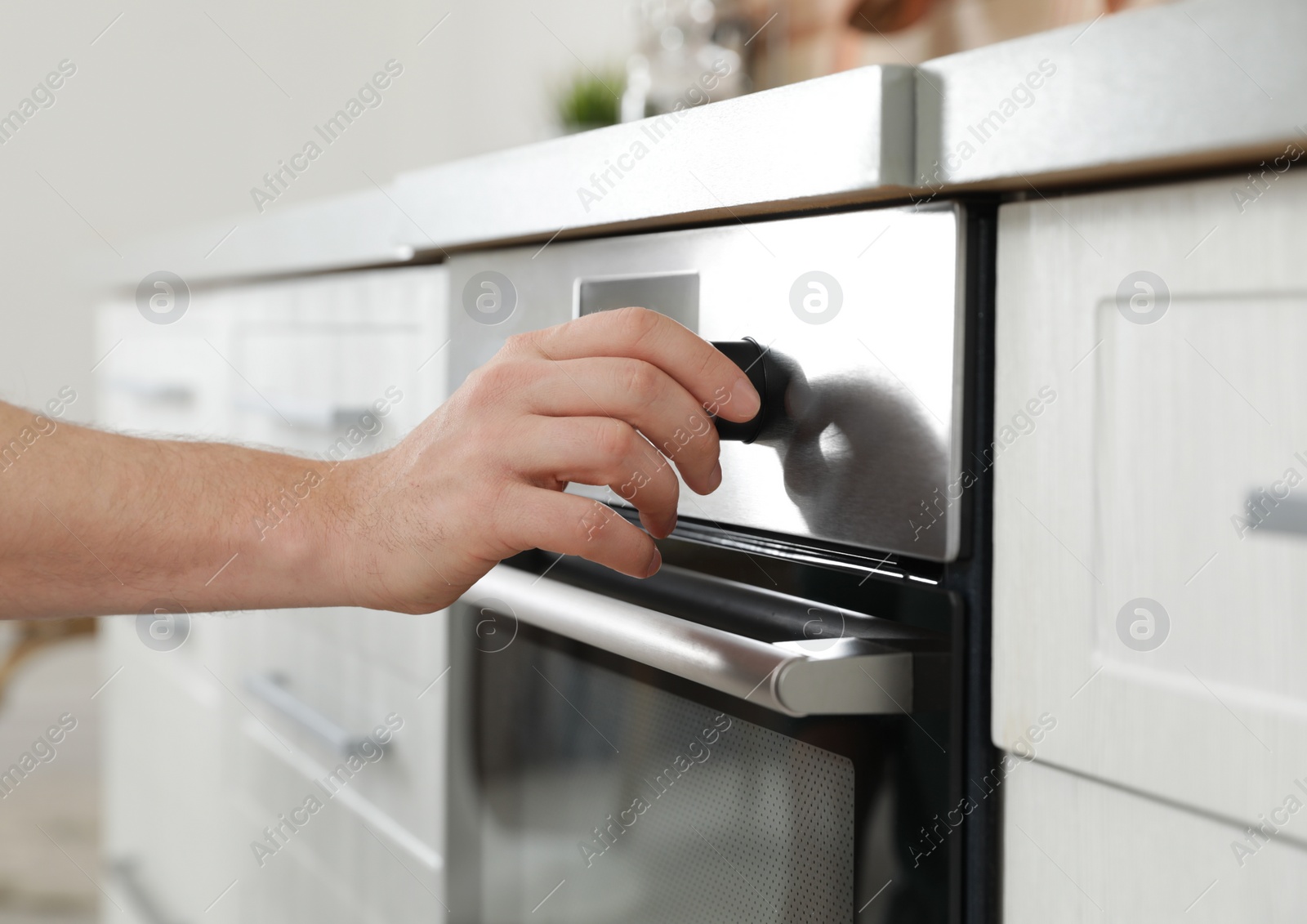 Photo of Man regulating cooking mode on oven panel in kitchen, closeup