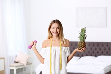 Photo of Happy slim woman with measuring tape, dumbbell and pineapple at home. Positive weight loss diet results