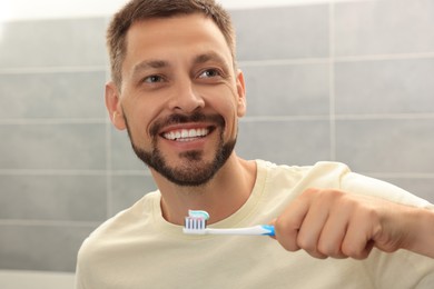 Photo of Man holding brush with toothpaste in bathroom