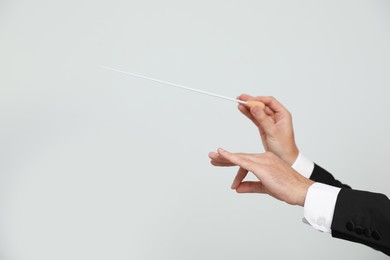 Professional conductor with baton on light grey background, closeup. Space for text