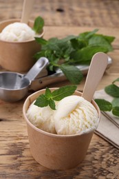 Photo of Paper cups with delicious ice cream and mint on wooden table