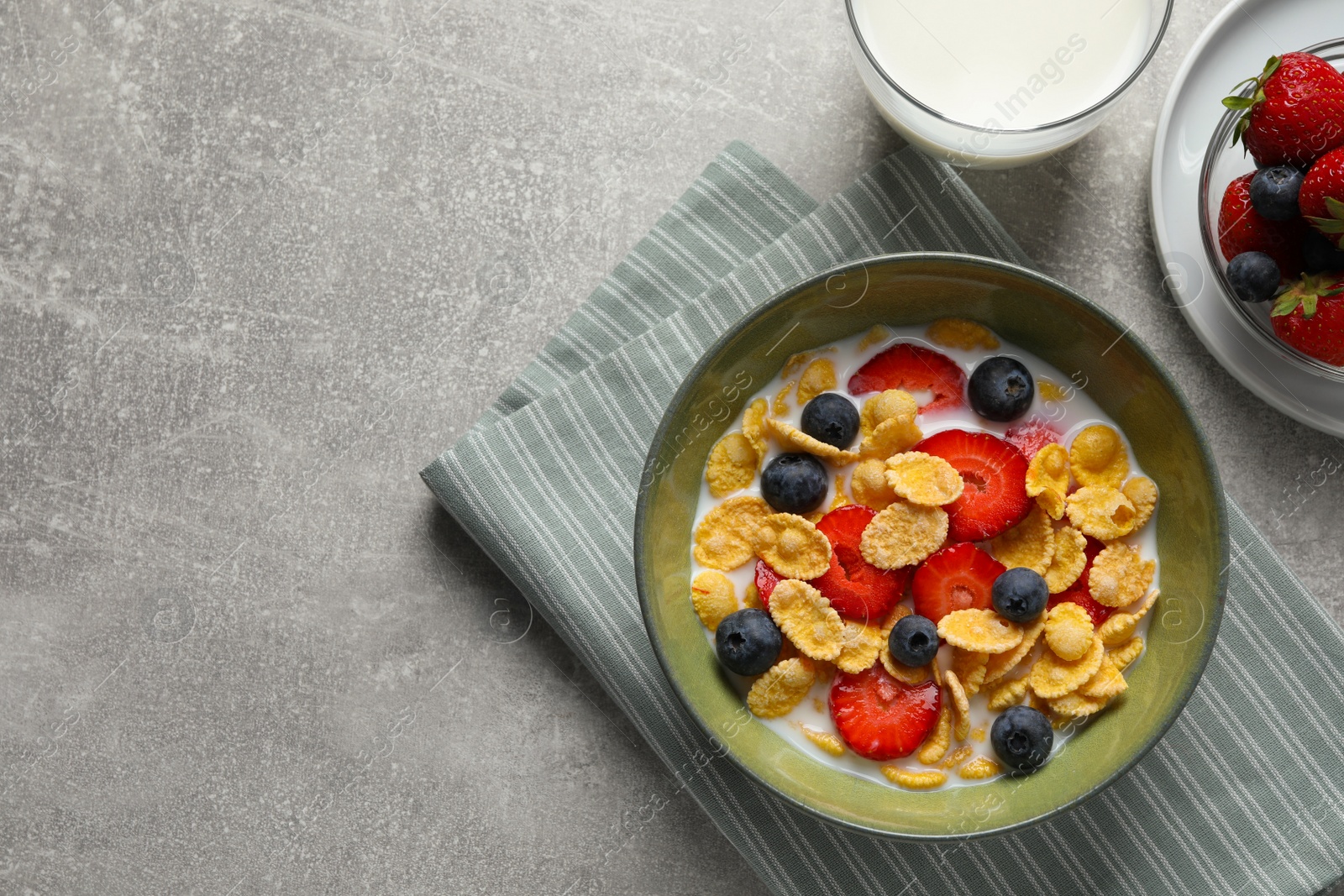 Photo of Corn flakes with berries in bowl served on grey table, flat lay. Space for text