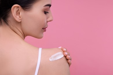 Photo of Beautiful woman with smear of body cream on her shoulder against pink background, back view. Space for text