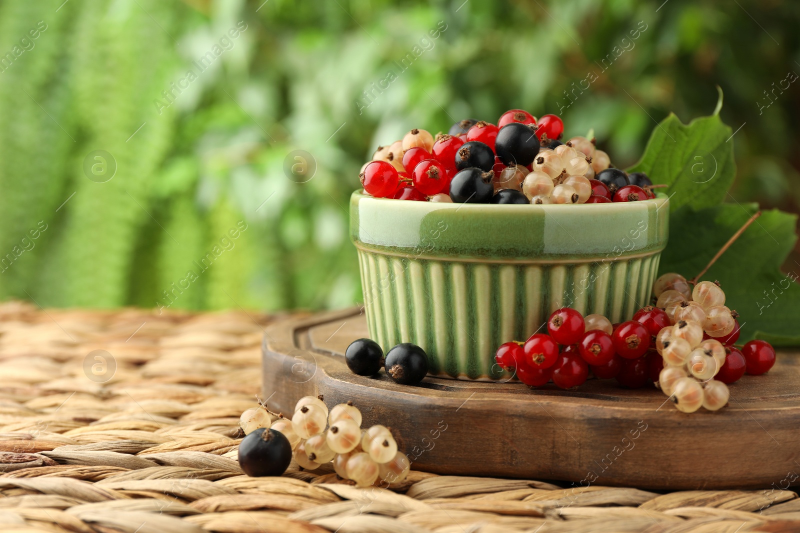 Photo of Different fresh ripe currants and green leaf on wicker surface outdoors, space for text