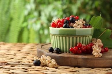 Different fresh ripe currants and green leaf on wicker surface outdoors, space for text