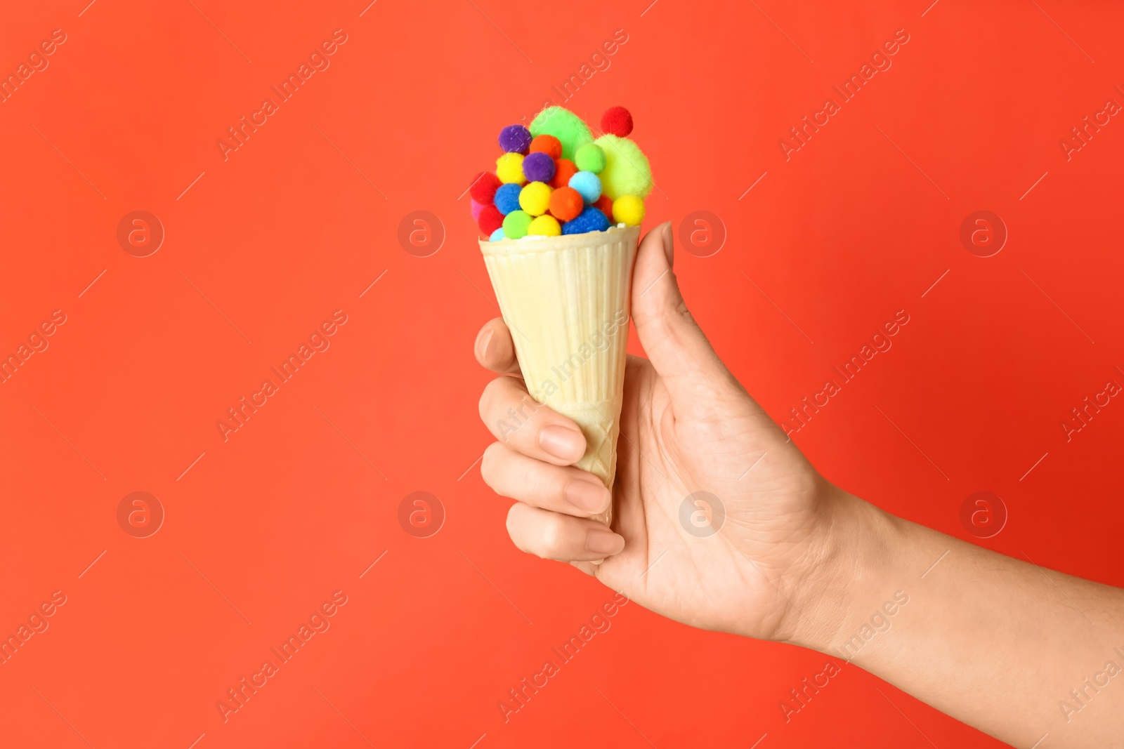 Photo of Woman holding ice cream waffle with fluffy balls on coral background, closeup