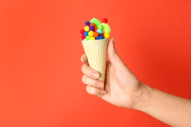 Woman holding ice cream waffle with fluffy balls on coral background, closeup