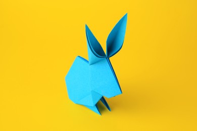 Origami art. Handmade light blue paper bunny on yellow background, closeup