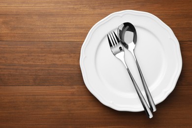Photo of Clean plate, spoon and fork on wooden table, top view. Space for text