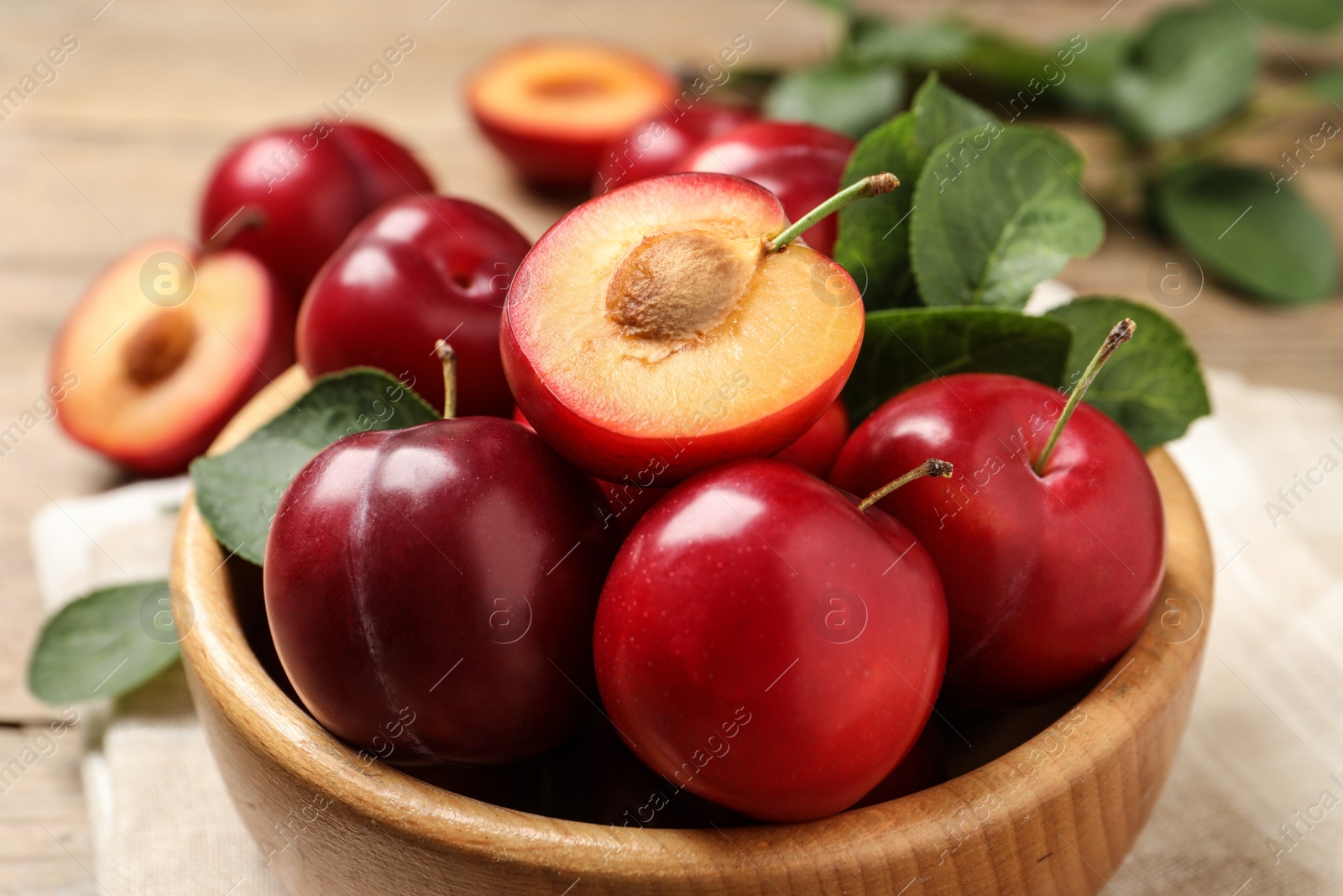 Photo of Delicious ripe cherry plums with leaves on wooden table, closeup