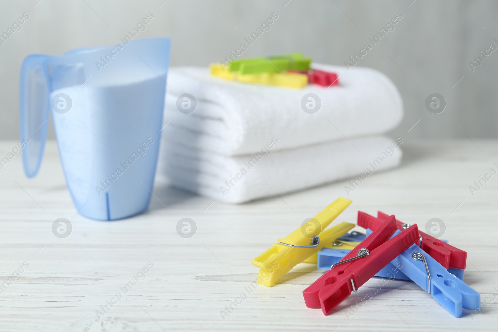 Photo of Colorful clothespins near detergent and towels on white wooden table