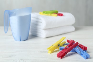 Photo of Colorful clothespins near detergent and towels on white wooden table