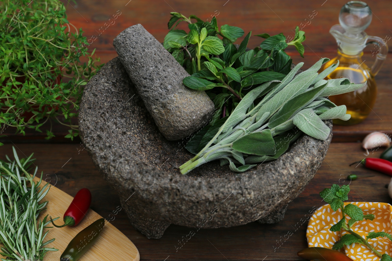 Photo of Mortar, different herbs, vegetables and oil on wooden table, closeup