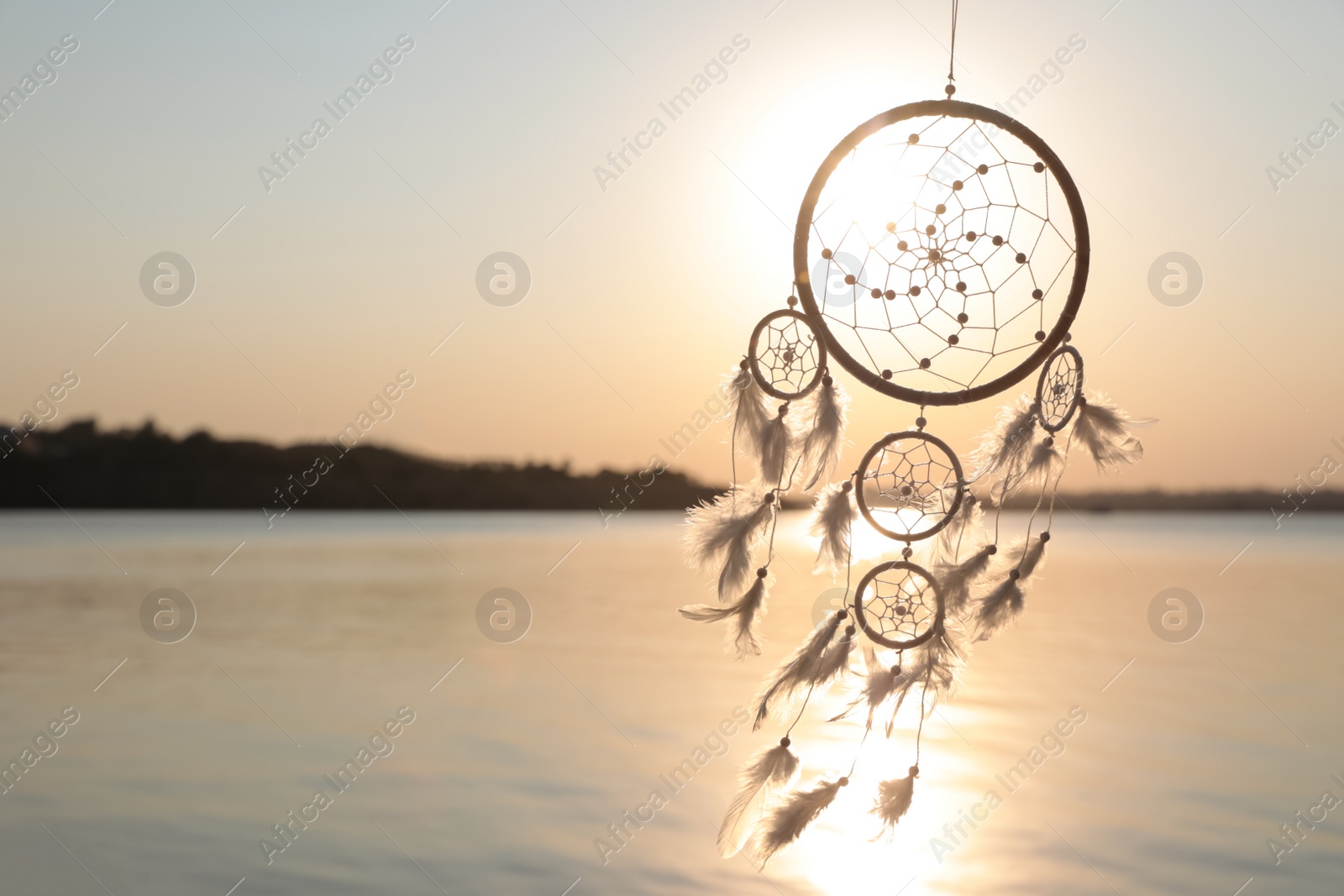 Photo of Beautiful handmade dream catcher near river at sunset. Space for text