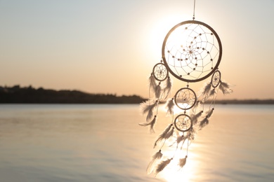 Photo of Beautiful handmade dream catcher near river at sunset. Space for text