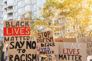 Photo of Protesters demonstrating different anti racism slogans outdoors. People holding signs with phrases, closeup view