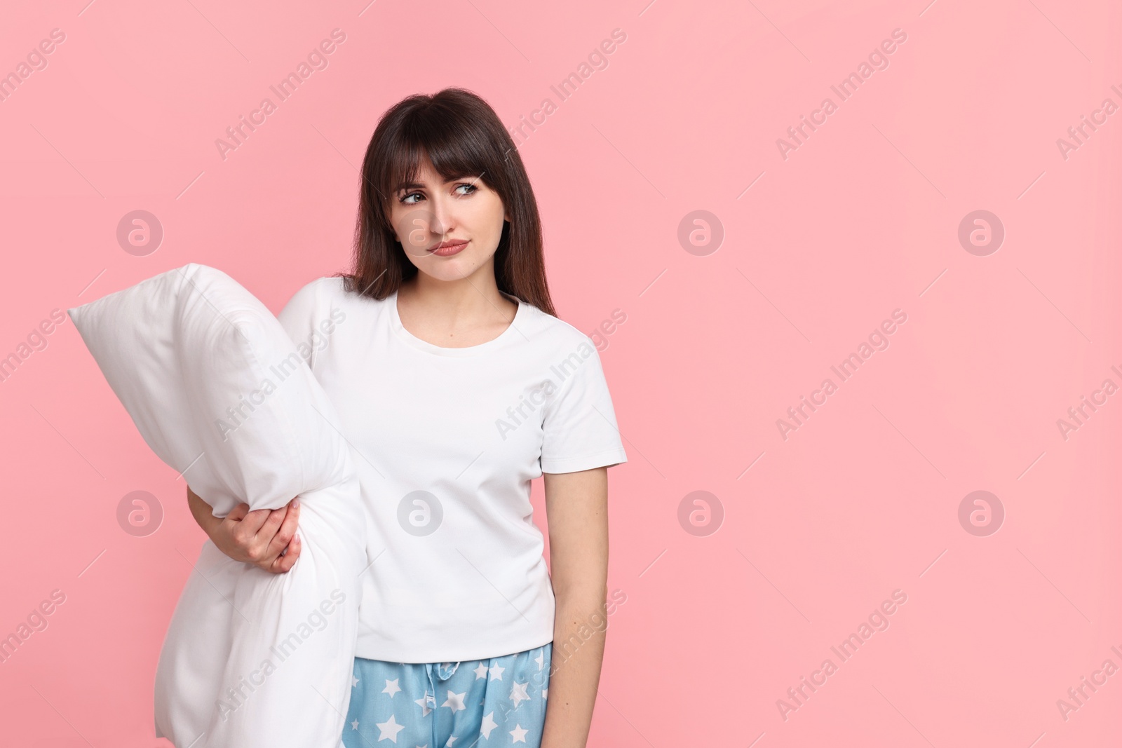 Photo of Woman in pyjama holding pillow on pink background, space for text