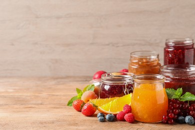 Jars with different jams and fresh fruits on wooden table. Space for text