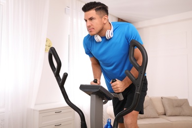 Man with headphones using modern elliptical machine at home