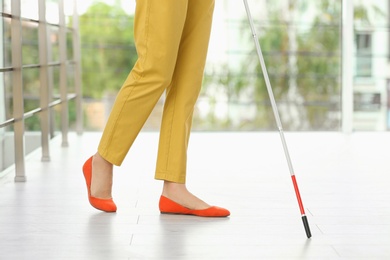 Photo of Blind person with long cane walking indoors, closeup