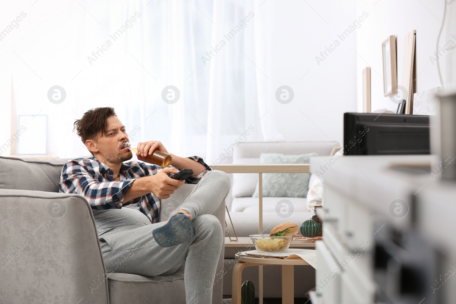 Photo of Lazy man with bottle of beer and chips watching TV at home