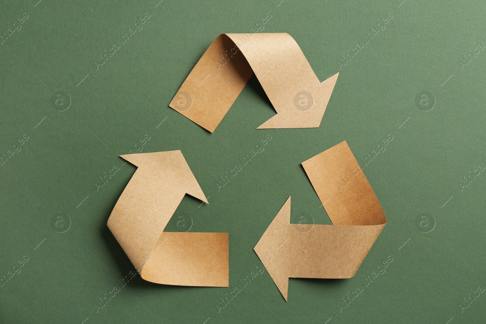 Photo of Recycling symbol cut out of kraft paper on green background, top view