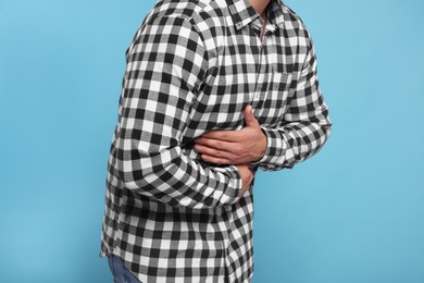 Photo of Man suffering from stomach pain on light blue background, closeup