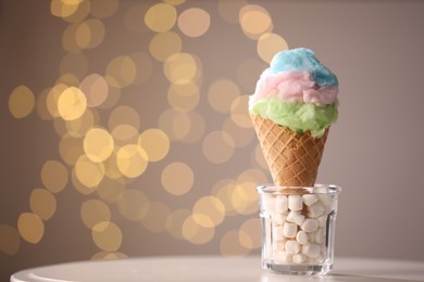 Photo of Sweet cotton candy in waffle cone on table against blurred lights, closeup. Space for text