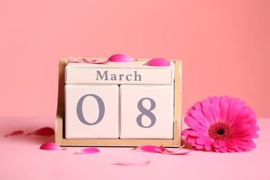 Photo of Wooden block calendar with flower on table against color background. International Women's Day