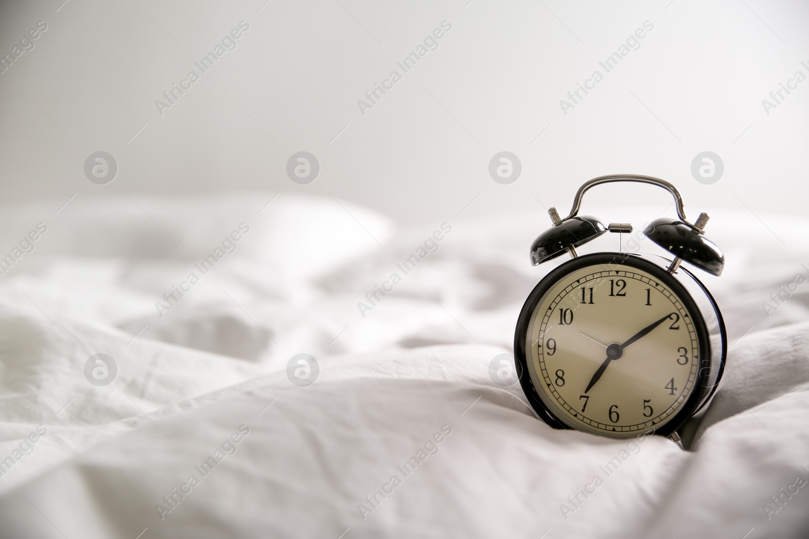 Photo of Alarm clock on bed, space for text. Morning time
