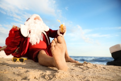 Photo of Santa Claus with cocktail relaxing on beach, space for text. Christmas vacation