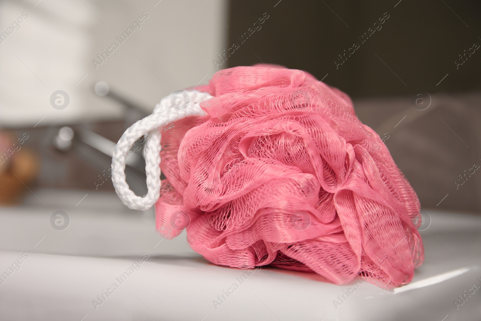 Photo of Pink shower puff on washbasin in bathroom, closeup