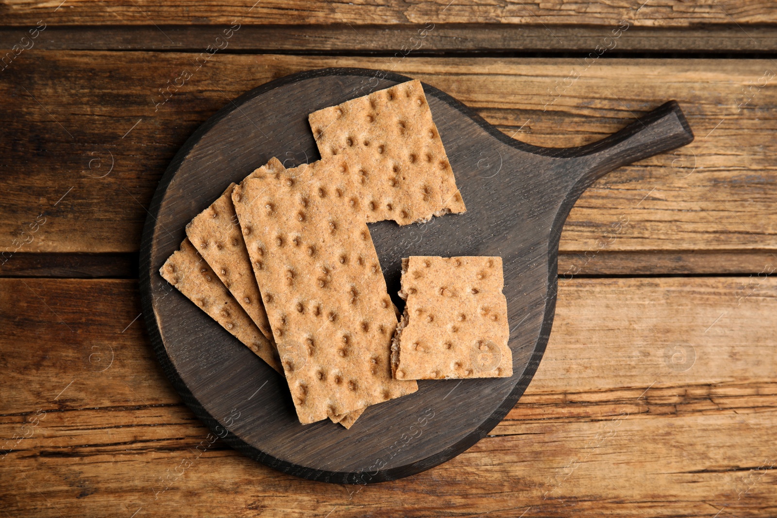 Photo of Board with fresh rye crispbreads on wooden table, top view