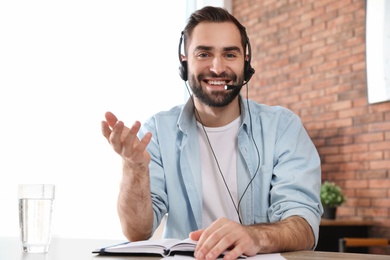 Photo of Young man with headset looking at camera and using video chat in home office