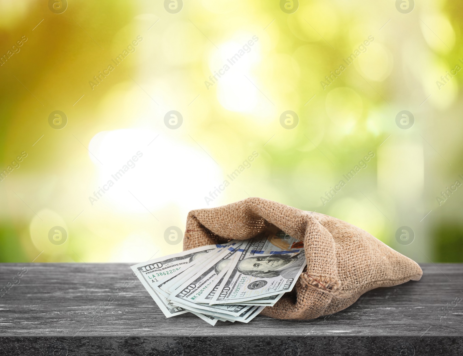 Image of Burlap bag with dollar banknotes on grey stone table against blurred green background